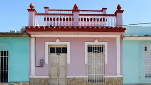 A two-story building with a pink facade, a stone base, and a balcony with red railings. - Hostal Tony y Daisy TRINIDAD (Trinidad)