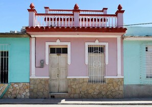 A two-story building with a pink facade, a stone base, and a balcony with red railings. - Hostal Tony y Daisy TRINIDAD (Trinidad)