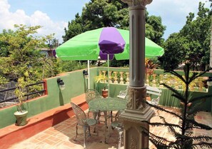 An outdoor patio with a table and chairs, surrounded by potted plants and a green umbrella. - Hostal Yoeslin y Denis TRINIDAD (Trinidad)
