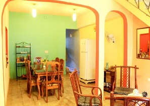 A dining area with a wooden table and chairs, a refrigerator, and a shelf with various items. - Hostal Yoeslin y Denis TRINIDAD (Trinidad)