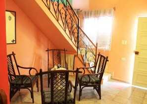 A dining area with a table and four chairs, a staircase with ornate railings, and a door in the background. - Hostal Yoeslin y Denis TRINIDAD (Trinidad)