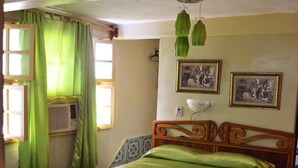 A bedroom with a wooden bed, green curtains, two wall-mounted pictures, and a ceiling light fixture. - La Moderna BARACOA (Baracoa)
