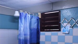A bathroom with a blue shower curtain, a window with blinds, and a tiled wall. - La Moderna BARACOA (Baracoa)