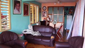 A living room with a brown leather sofa, a wooden chair, and a dining table with chairs. There are framed pictures on the wall and a clock. - La Moderna BARACOA (Baracoa)