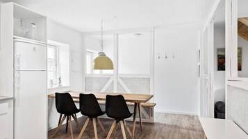 A modern kitchen with white cabinetry, a wooden dining table with black chairs, and a yellow pendant light.
