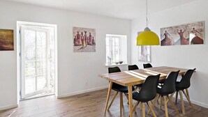 Un comedor con una mesa de madera y sillas negras, una lámpara colgante amarilla y obras de arte en las paredes.