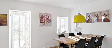 A dining area with a wooden table and black chairs, a yellow pendant light, and artwork on the walls.