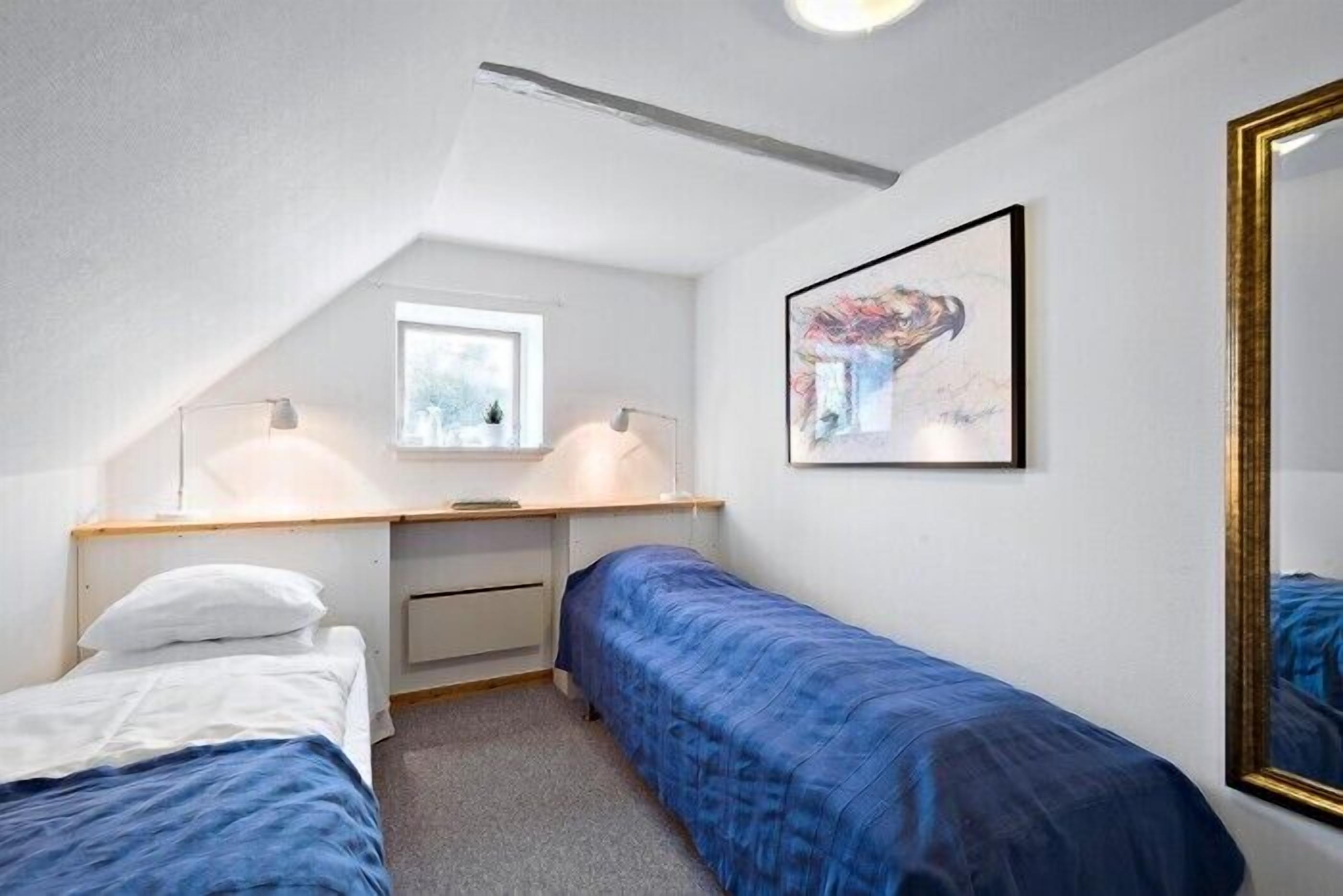 Una habitación pequeña y luminosa con una cama individual, un escritorio con silla, una ventana y un cuadro en la pared.