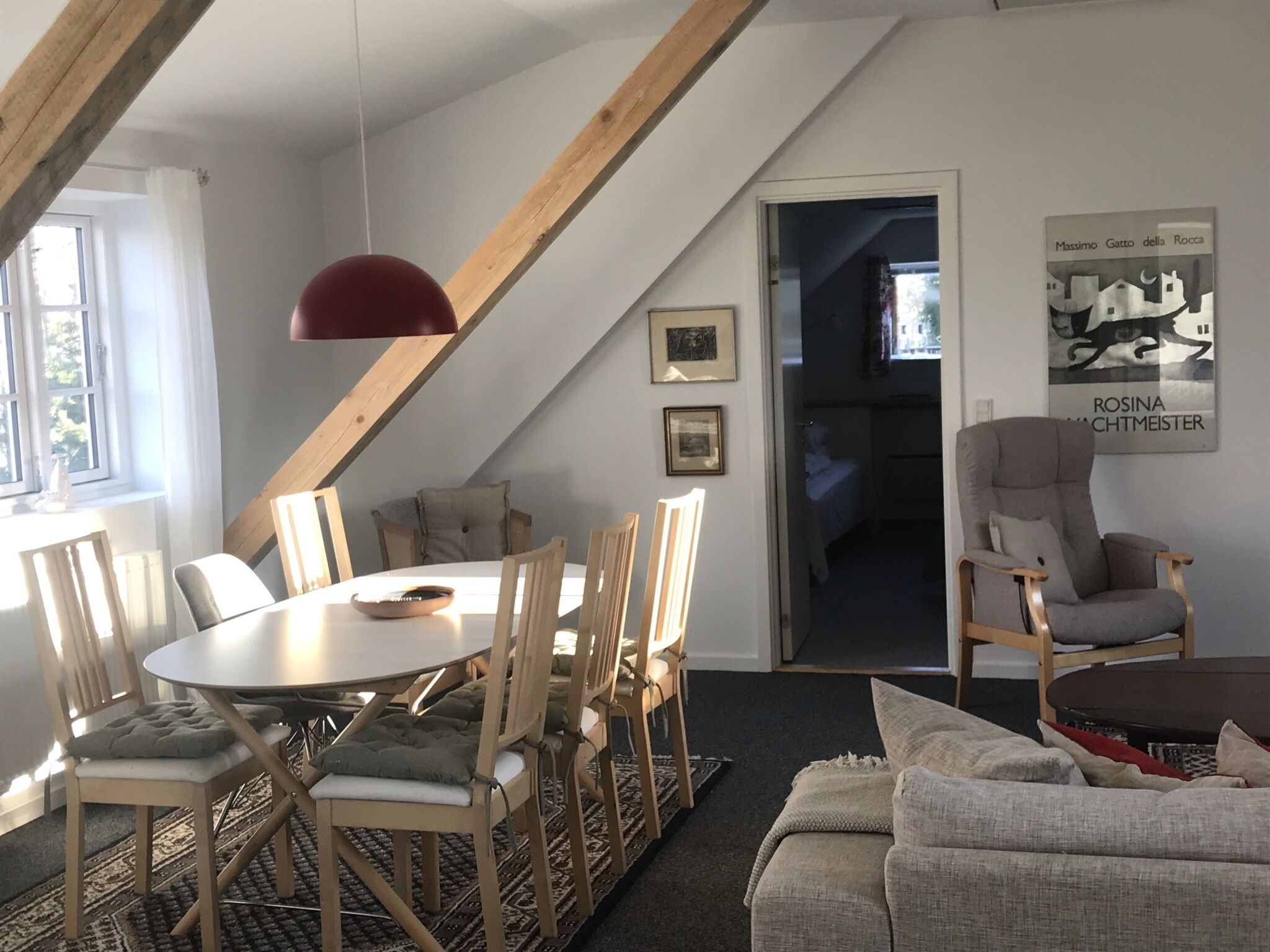 Zona pranzo con tavolo rotondo e sedie, una lampada a sospensione rossa e vista su una camera da letto.