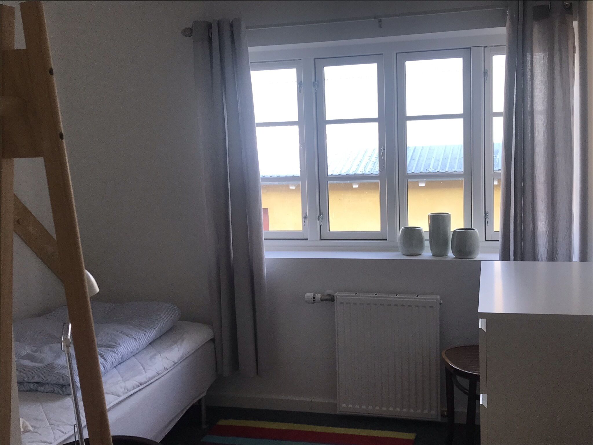 Une petite pièce avec un lit, un radiateur et une fenêtre avec des rideaux.
