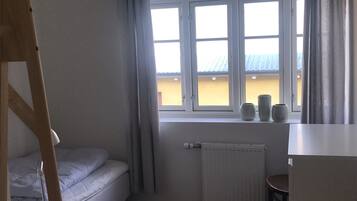 Une petite pièce avec un lit, un radiateur et une fenêtre avec des rideaux.