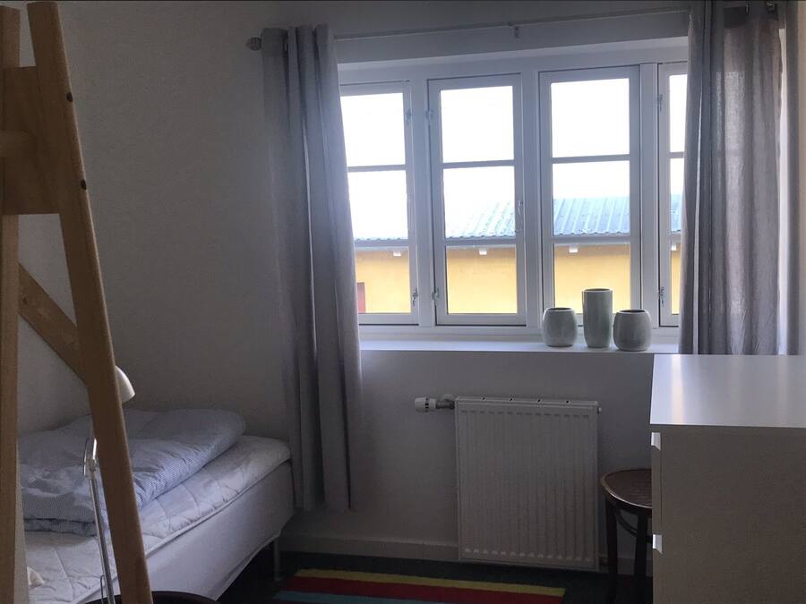 Une petite pièce avec un lit, un radiateur et une fenêtre avec des rideaux.