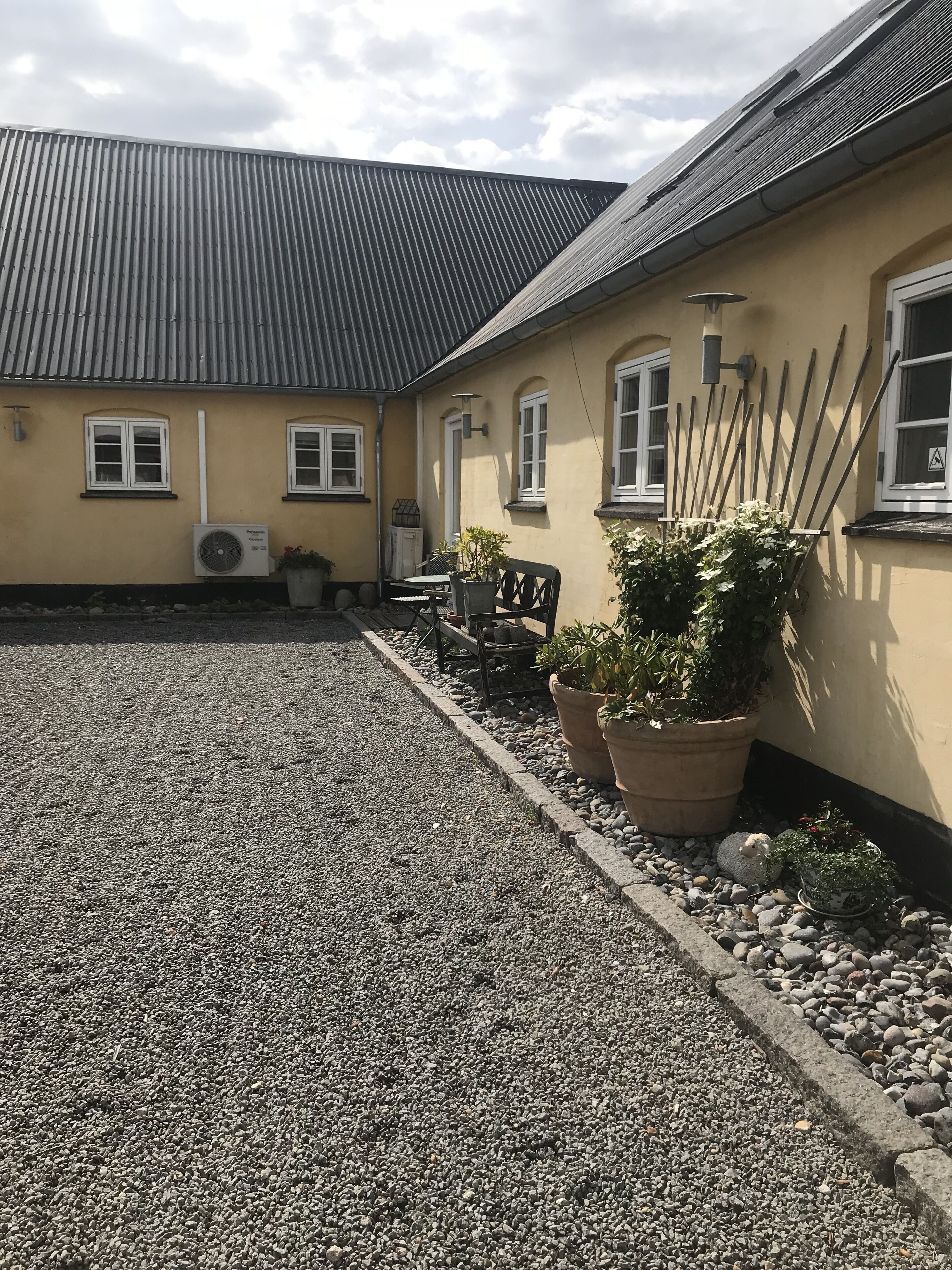 A building with a yellow exterior, a gravel driveway, and potted plants.