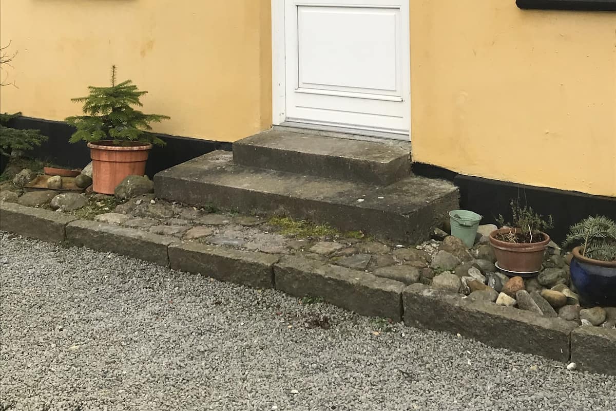 A yellow house with a white door, a window, and a small porch with steps.