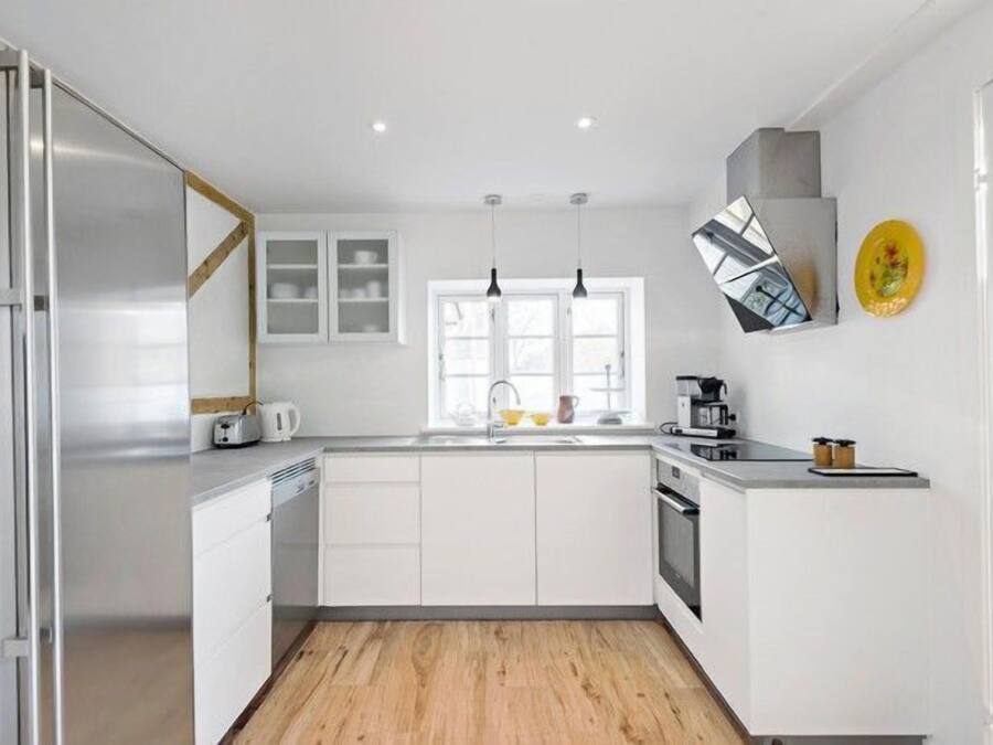 Una cocina moderna con armarios blancos, piso de madera, horno empotrado, pileta y estufa.