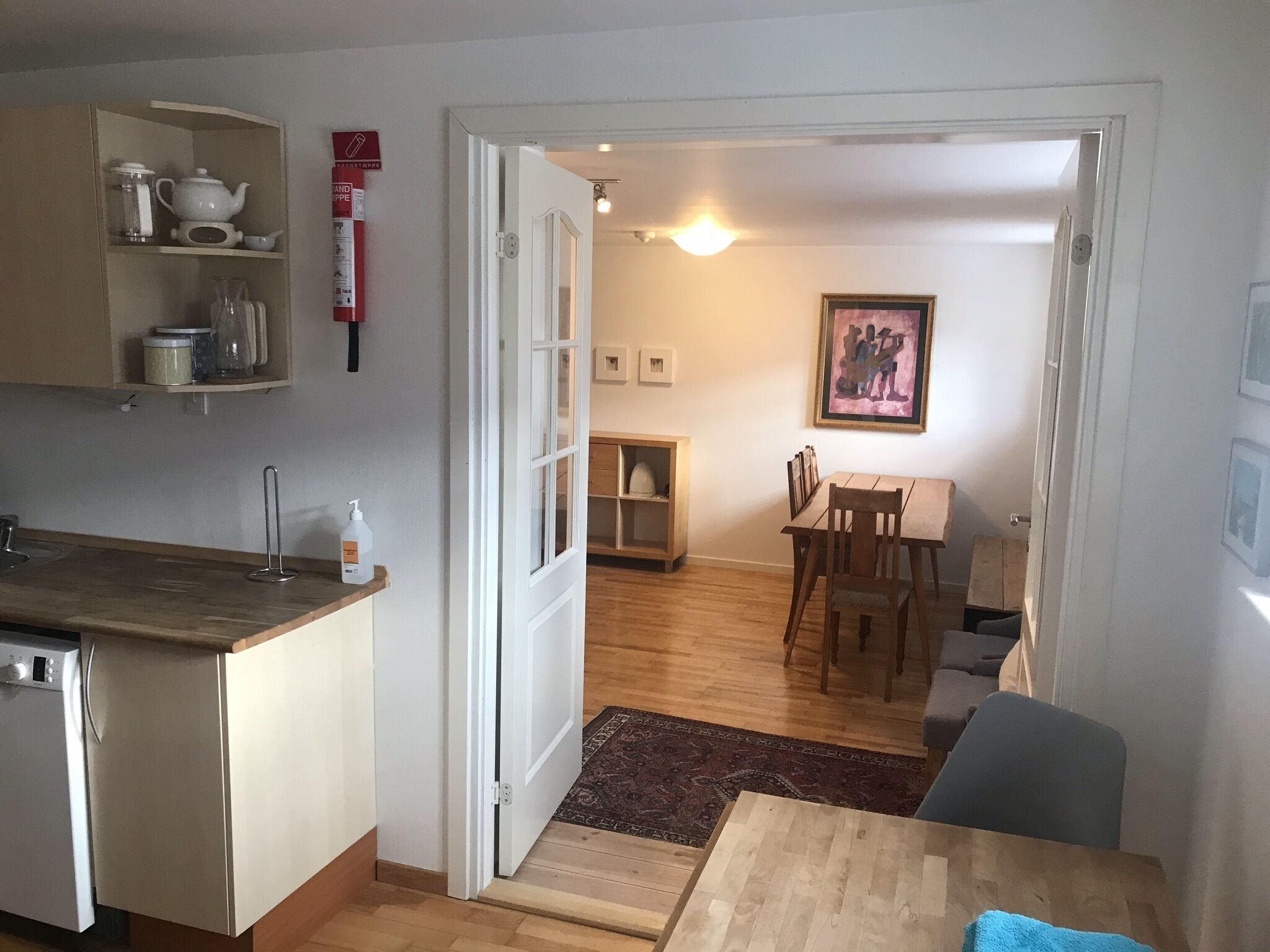 A compact kitchen with a refrigerator, a sink, and a countertop. There is a dining area with a table and chairs, and a small rug on the floor.