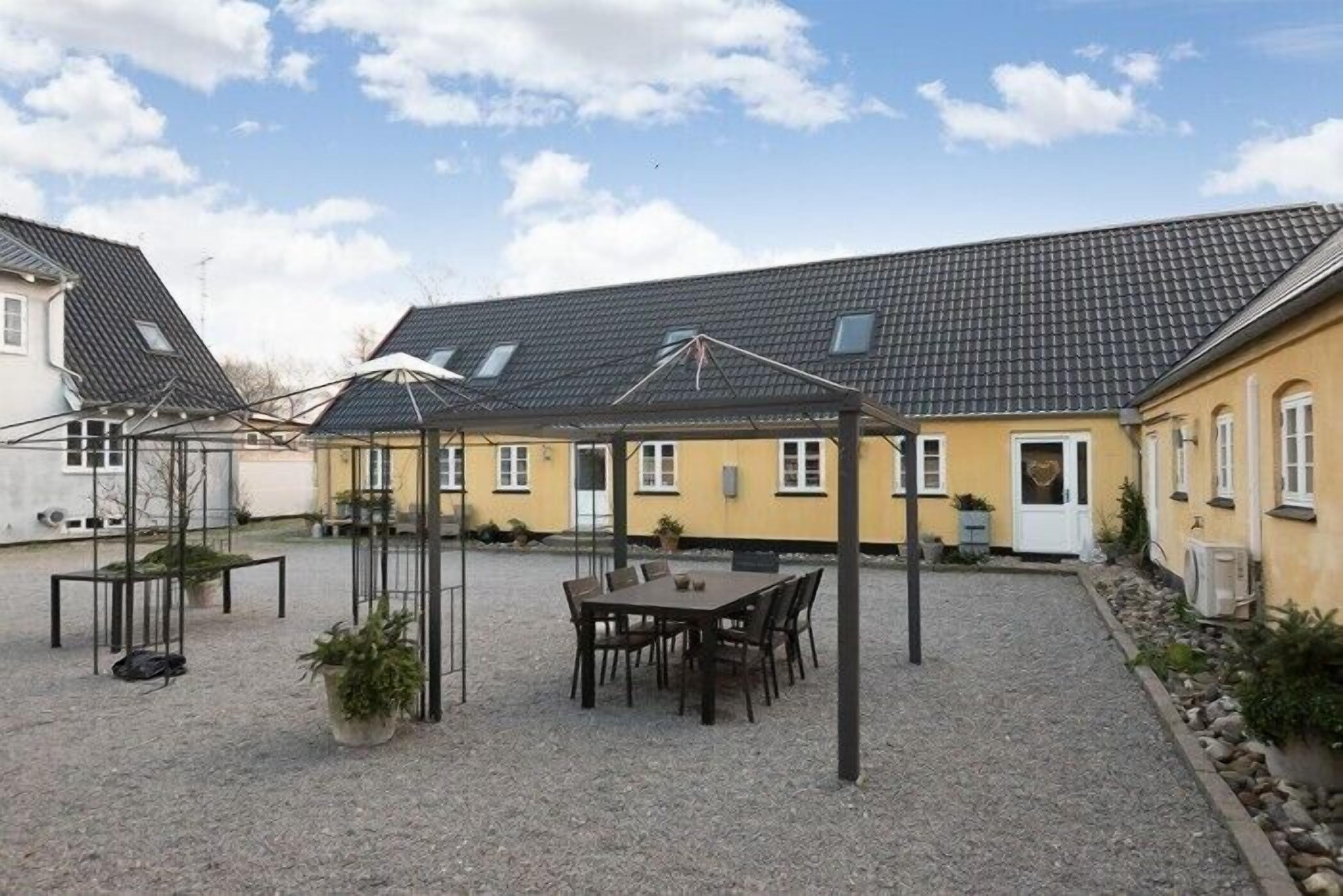 A courtyard with a table and chairs, surrounded by buildings with tiled roofs and a gravel ground.