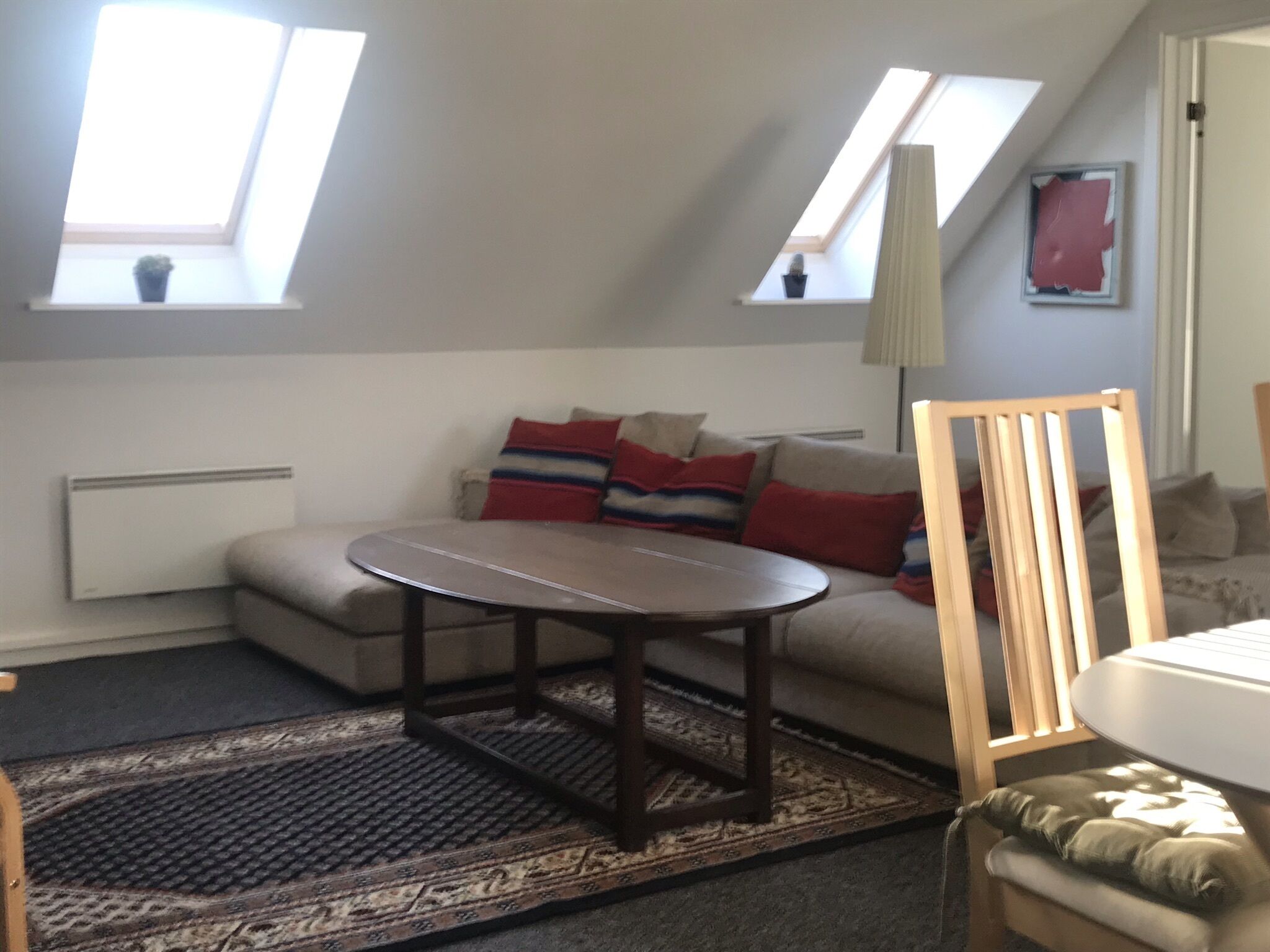 A cozy living room with a sofa, a round coffee table, and a wooden chair. There are skylights on the ceiling, a radiator, and a rug on the floor.