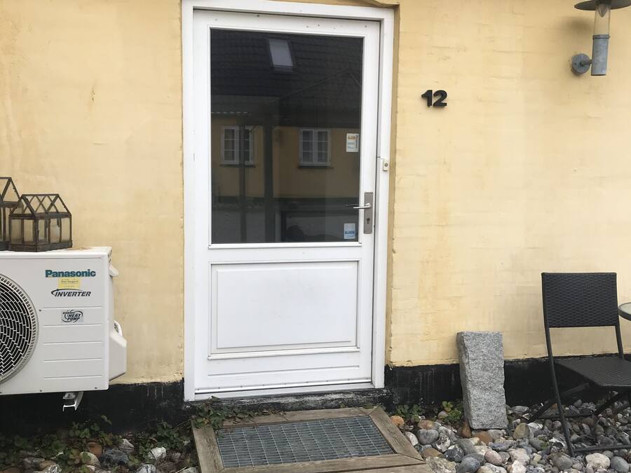 Un edificio con una puerta blanca, el número '12' en la pared y una unidad Panasonic inverter en el exterior.