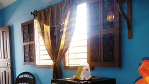 Una habitación con paredes azules, una ventana con cortinas, un ventilador de techo y una mesa con un bolso y un libro.