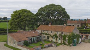 A stone building with a tiled roof, surrounded by a gravel driveway and a grassy area.