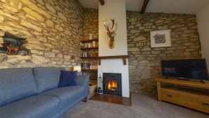 A stone-walled living room with a fireplace, a sofa, and a television on a wooden stand.