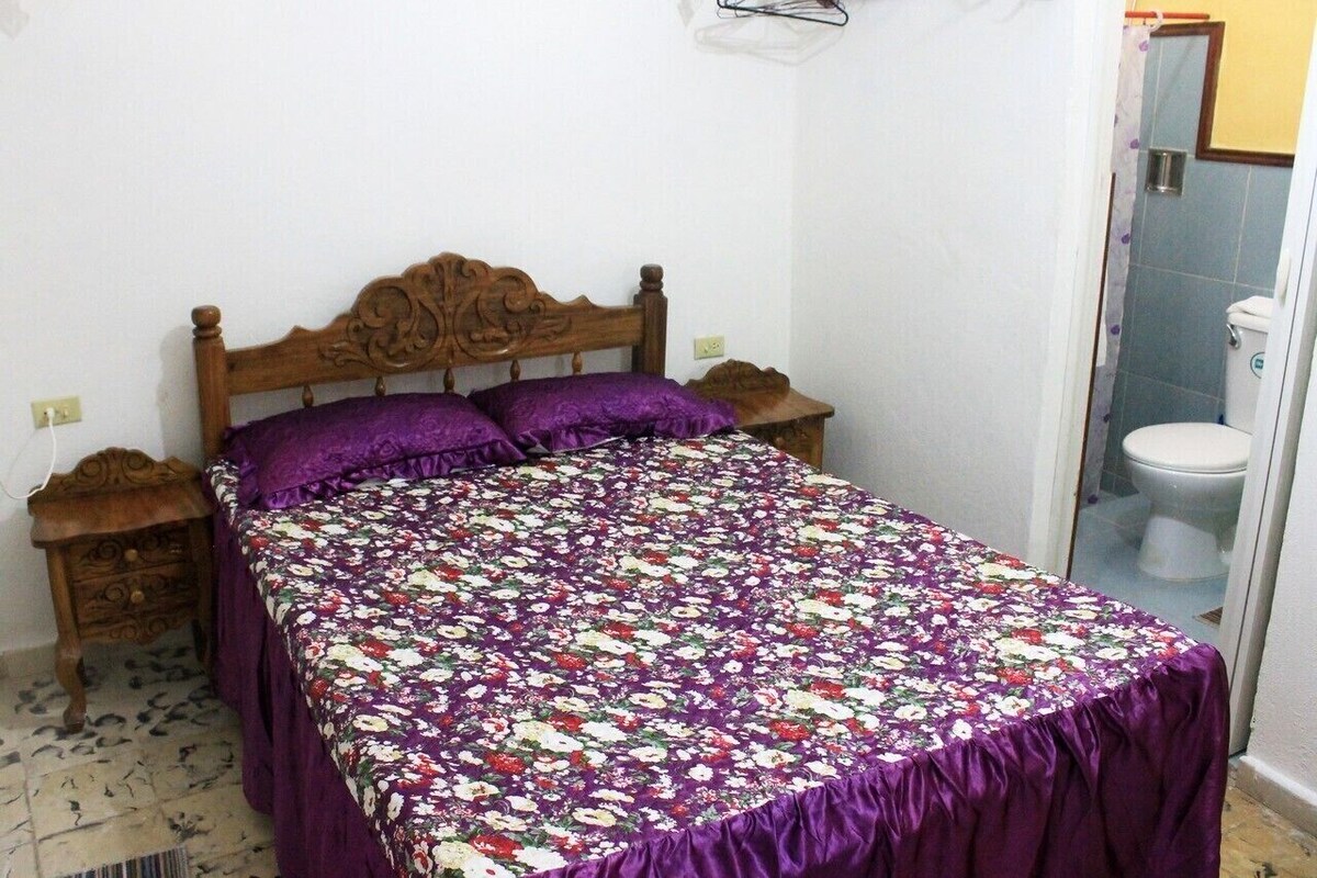 A bedroom with a wooden bed, purple bedding, and a small bedside table.