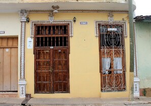 A building with two large wooden doors and a window with decorative metal bars. - Hostal Ricardo Leon TRINIDAD (Trinidad)