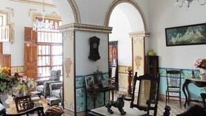 Een kamer met een grote gewelfde deuropening, een kroonluchter, een houten kast en een ingelijst schilderij aan de muur.