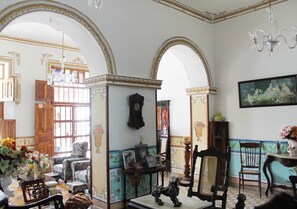 A room with a large arched doorway, a chandelier, a wooden cabinet, and a framed picture on the wall. - Hostal Ricardo Leon TRINIDAD (Trinidad)
