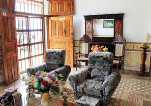 A traditional room with patterned armchairs, a wooden door with intricate designs, and a tiled floor. - Hostal Ricardo Leon TRINIDAD (Trinidad)