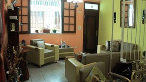 A living room with a sofa, armchairs, a coffee table, and a TV. There is a window with blinds and a door with a mirror. - Hostal Yolanda HABANA VIEJA (Havana)