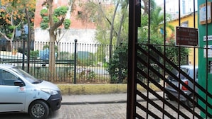 A gated entrance with a car parked in front, a metal fence, and a building with a green wall and a sign in Spanish. - Hostal Yolanda HABANA VIEJA (Havana)