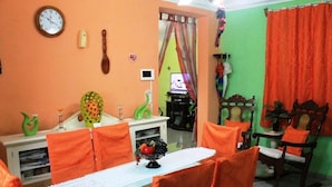 A dining area with a table set for four, surrounded by orange chairs, a clock on the wall, and a television in the background. - Hostal Yolanda HABANA VIEJA (Havana)