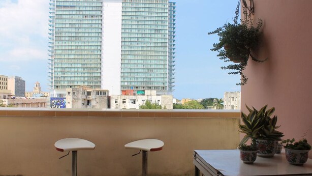 Een balkon met twee barkrukken, een tafel en planten in potten.