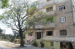 A multi-story building with a staircase leading to the entrance, a tree in front, and a person standing near the building. - Sophi's House VEDADO (Havana)