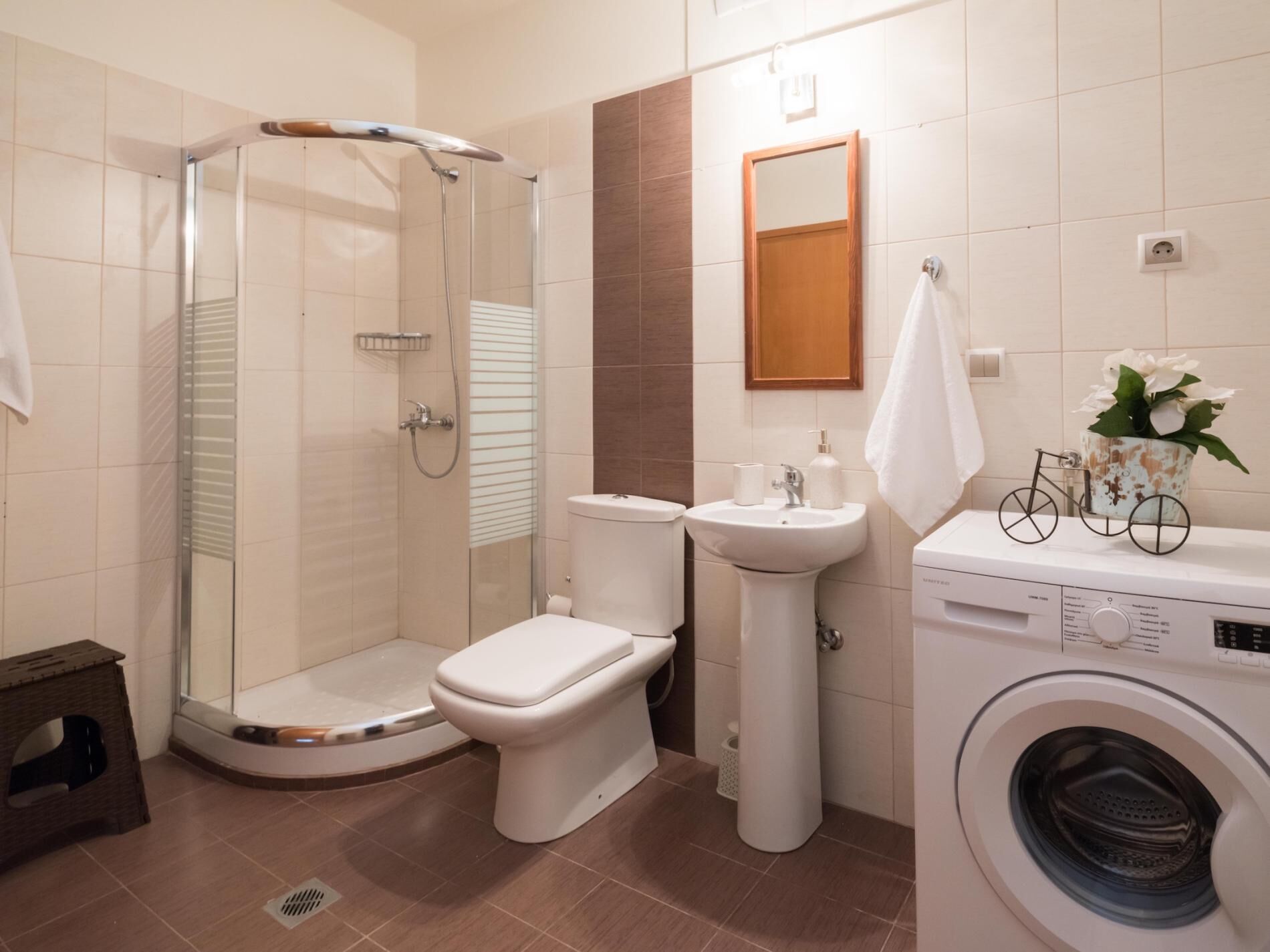 A bathroom with a glass-enclosed shower, a toilet, a sink, and a washing machine.
