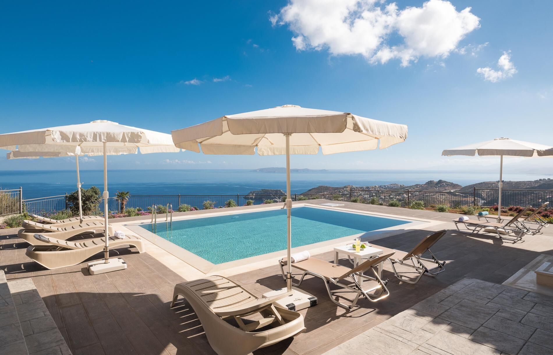 A poolside area with lounge chairs and umbrellas, overlooking a body of water and distant land.