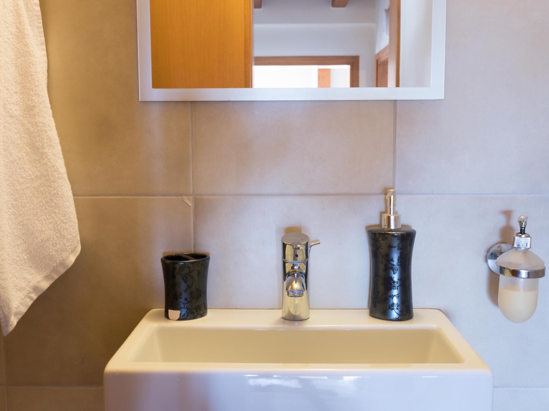 A bathroom with a white sink, a mirror, and a towel hanging on the wall.
