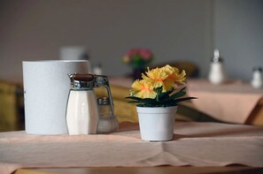 A table with a pitcher, salt and pepper shakers, and a small potted plant with yellow flowers. - Pension am See (Schluchsee)