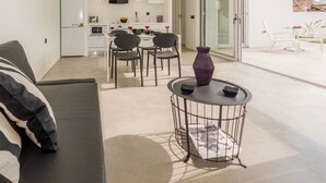 A modern living area with a sofa, a dining table with chairs, a kitchen in the background, and a balcony with a table and chairs. - Paradiso II (Malevizi)