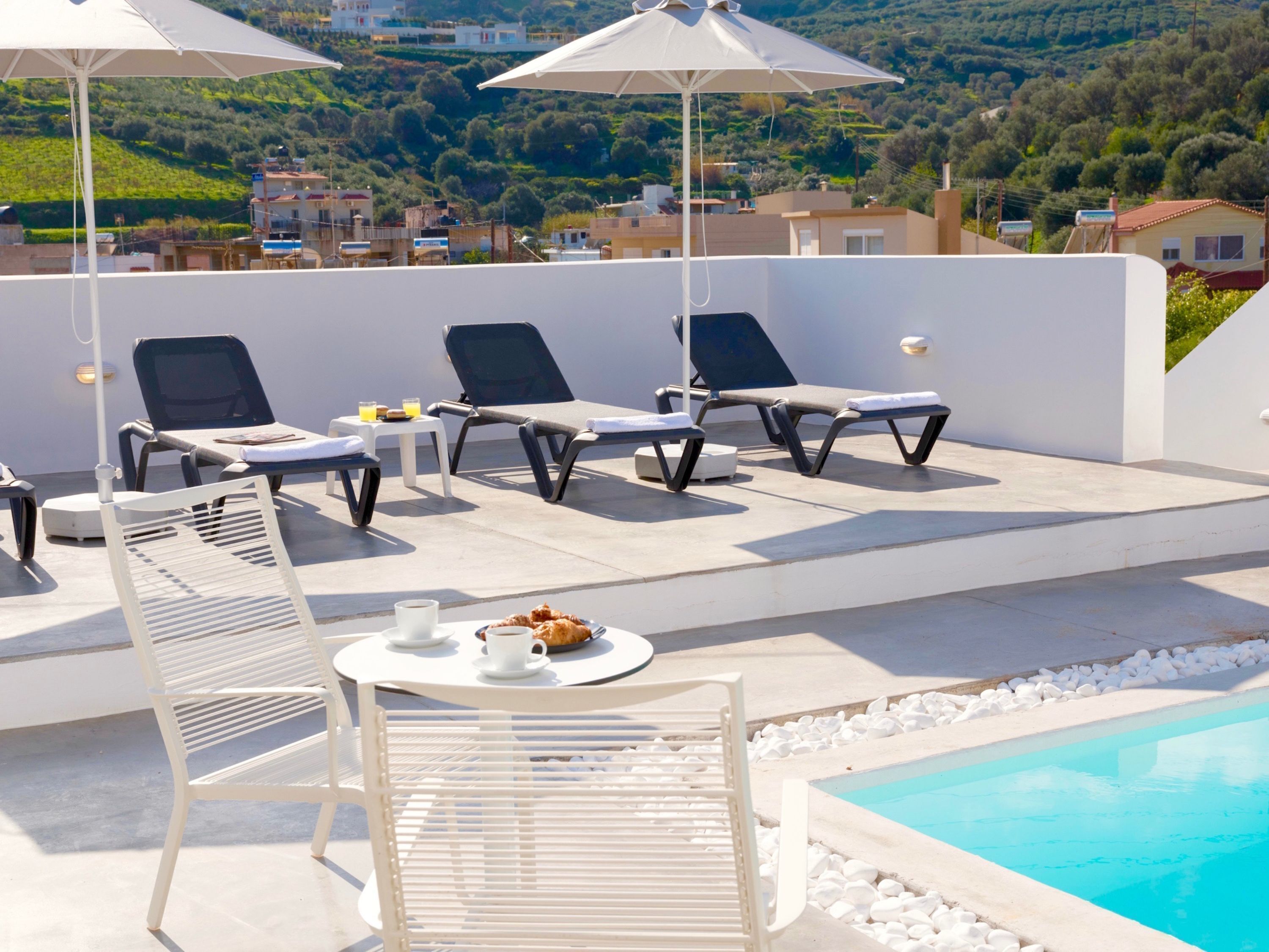 Une terrasse sur le toit avec des chaises longues, une piscine et une table où sont servis les articles du petit-déjeuner.