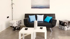 Ein modernes Wohnzimmer mit einem schwarzen Ledersofa, zwei weißen Tischen und einem gerahmten Landschaftsbild an der Wand.