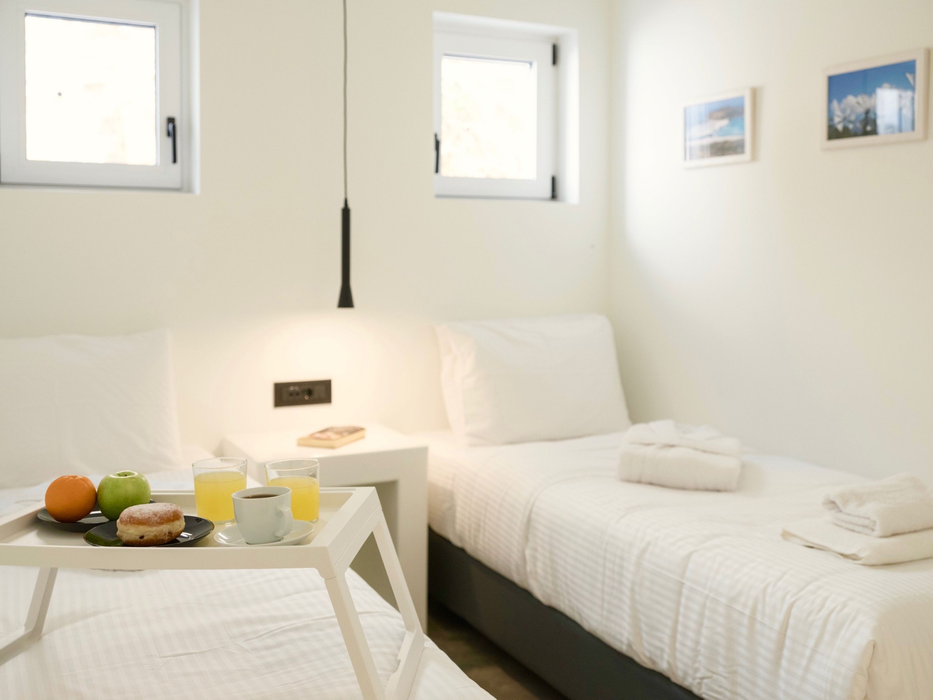 A hotel room with a bed, bedside table with breakfast items, and two windows.