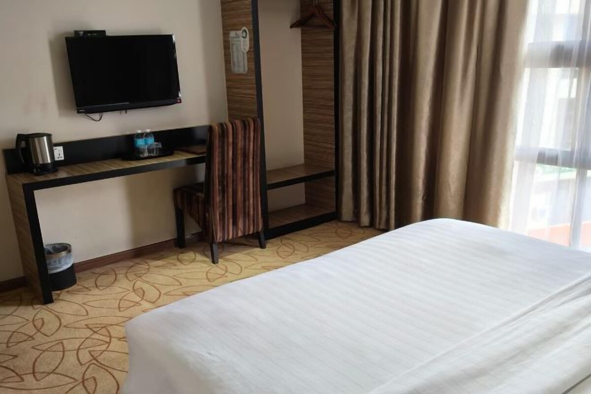 Habitación de hotel con cama, televisión montada en la pared, escritorio con cafetera y una silla.