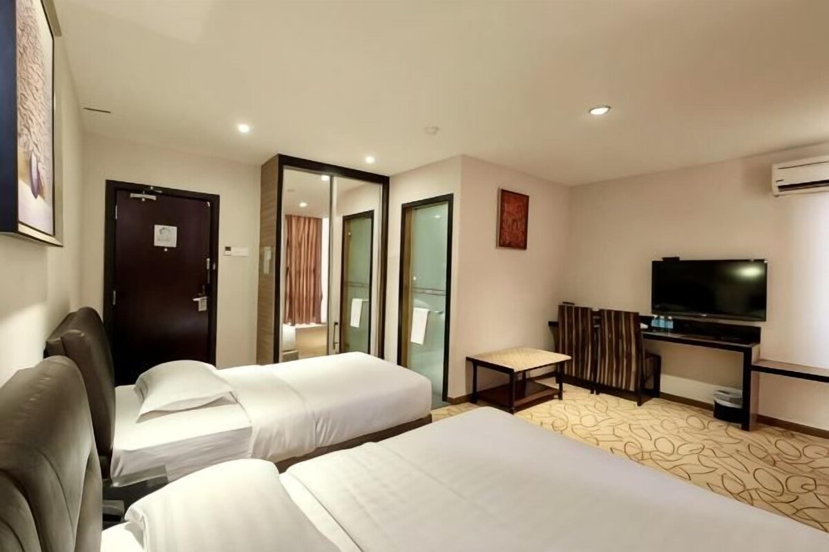 A hotel room with two beds, a TV, a desk, and a mirror.