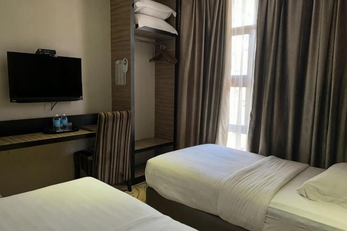 Habitación de hotel con dos camas, televisión, perchero y ventana con cortinas.