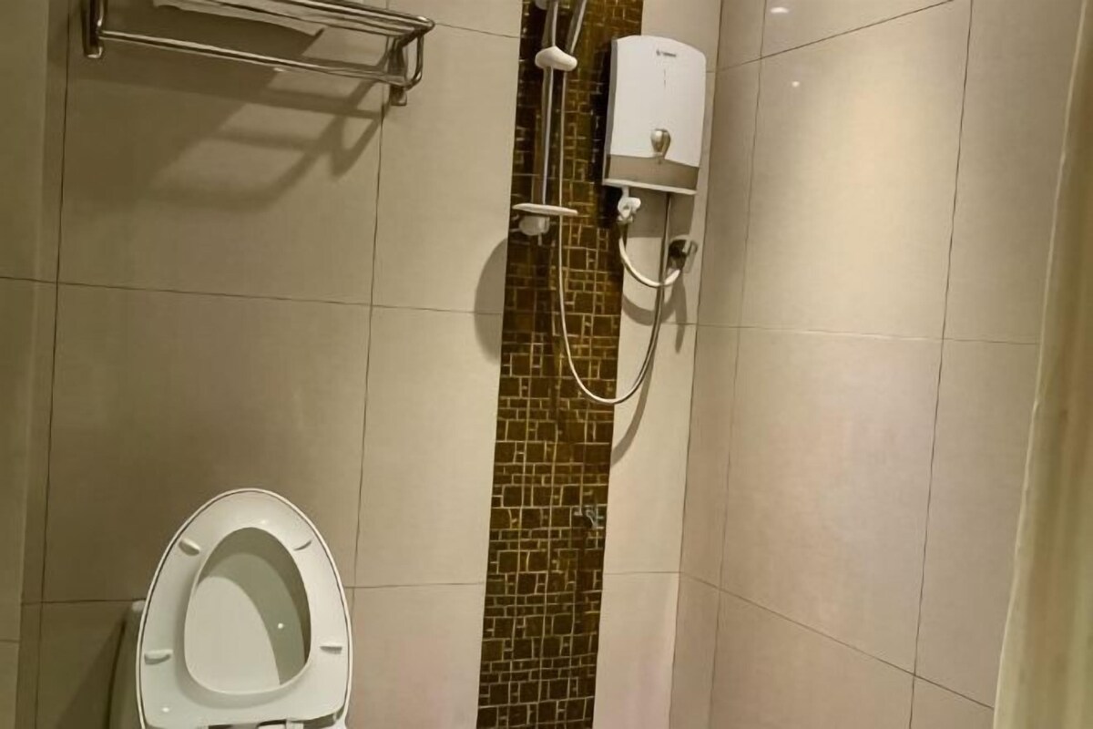 A bathroom with a toilet, a shower area with a handheld showerhead, and a wall-mounted water heater.