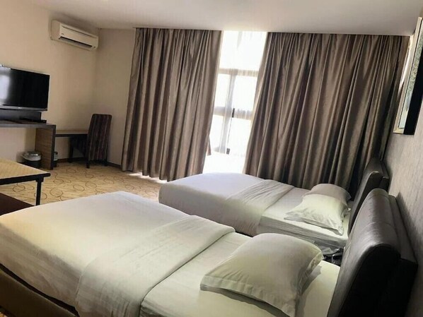 A hotel room with two beds, a TV, a desk, and a window with curtains. - Milano Hotel (Kluang)