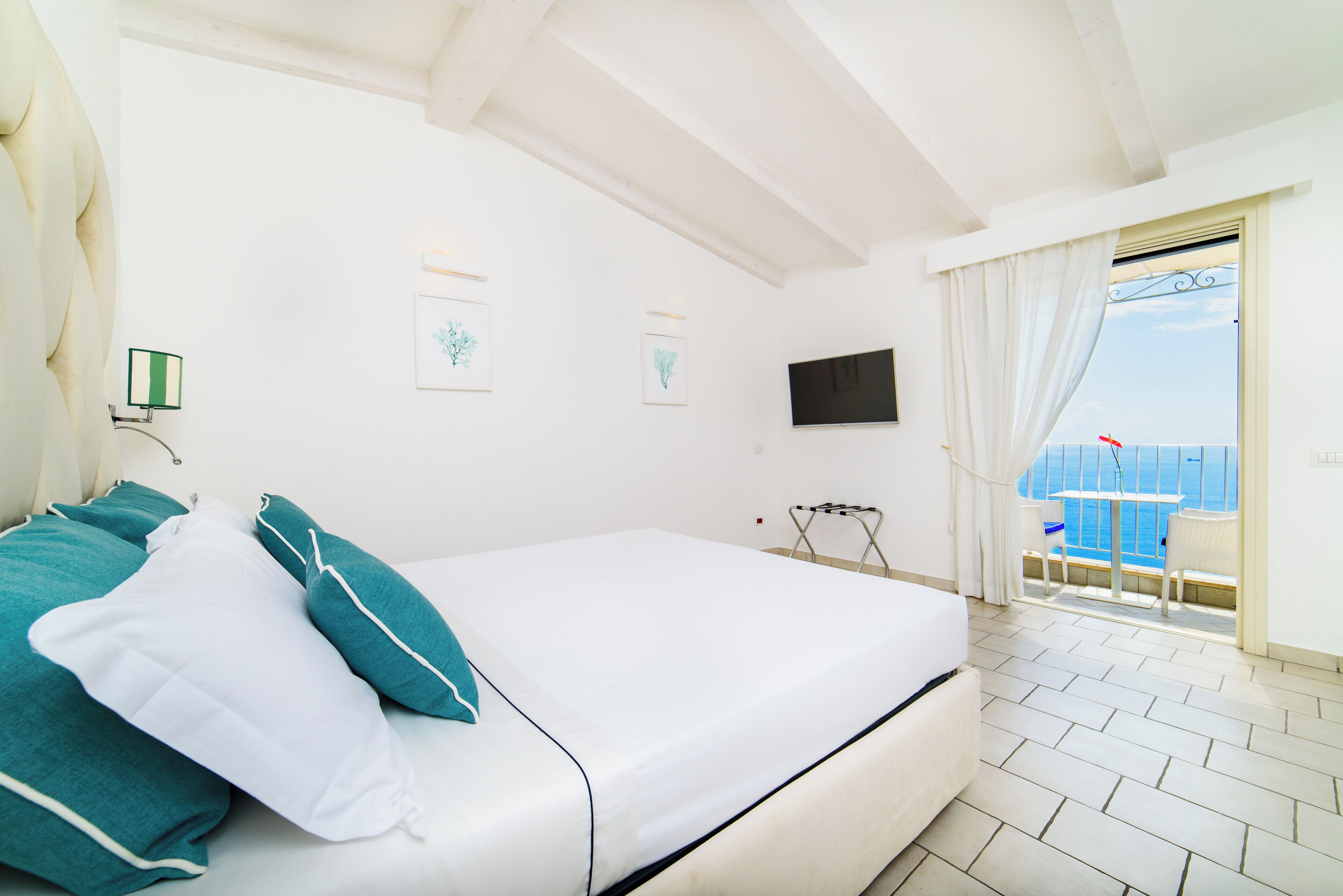 Un dormitorio con cama, televisor y balcón con vista al mar.